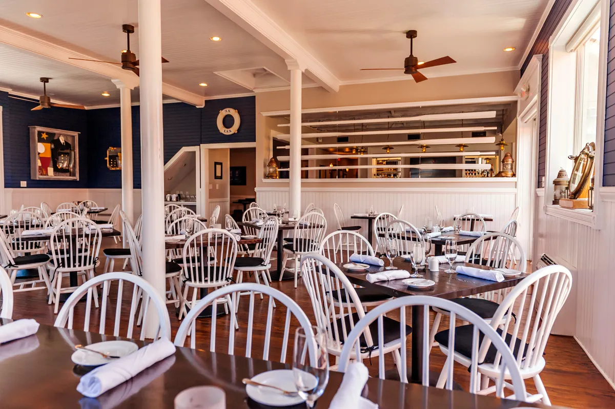 This image presents a stylish dining setup with white wooden chairs and dark wooden tables, complemented by decorative wall art. The ambiance is relaxed and welcoming, ideal for shared meals and social gatherings.