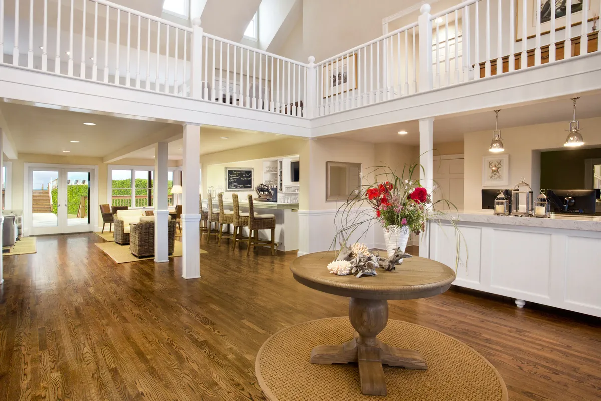 This image features a central round dining table adorned with a vibrant floral arrangement, set within an open-concept kitchen area. Large windows flood the space with natural light, creating a bright, inviting atmosphere perfect for gathering and sharing meals. The visible kitchen area showcases ample prep space and modern amenities.