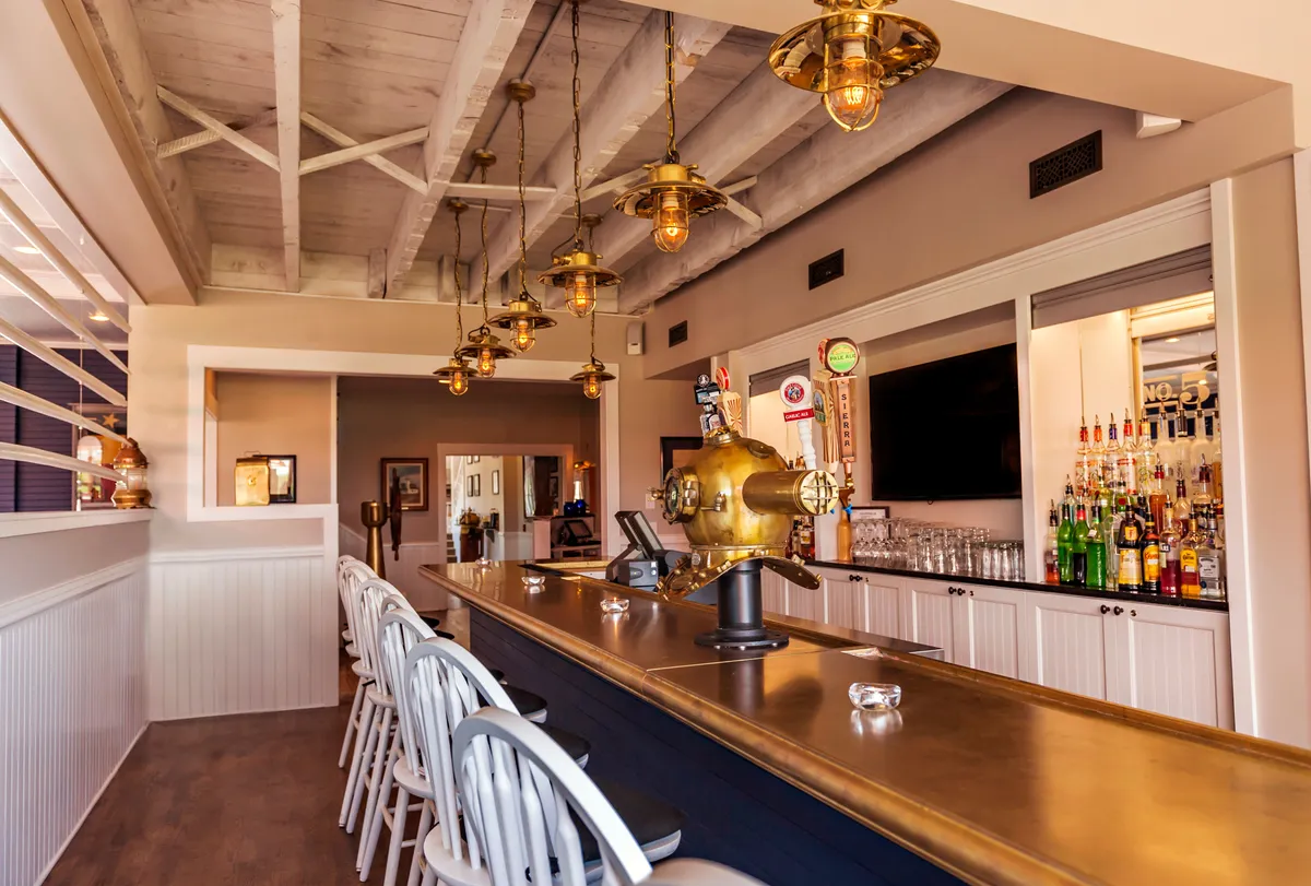 An inviting interior bar area featuring a sleek counter, stylish hanging light fixtures, and a well-stocked shelf of bottles. Guests are seen socializing and relaxing, evoking a sense of community and leisure after a day of activities.