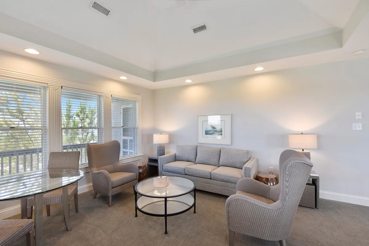 A serene seating nook with a comfortable sofa, round coffee table, and large windows that bathe the space in gentle daylight. The scene invites quiet reading, relaxed chats, or enjoying a board game, with a calm ambiance perfect for unwinding after a day by the sea.
