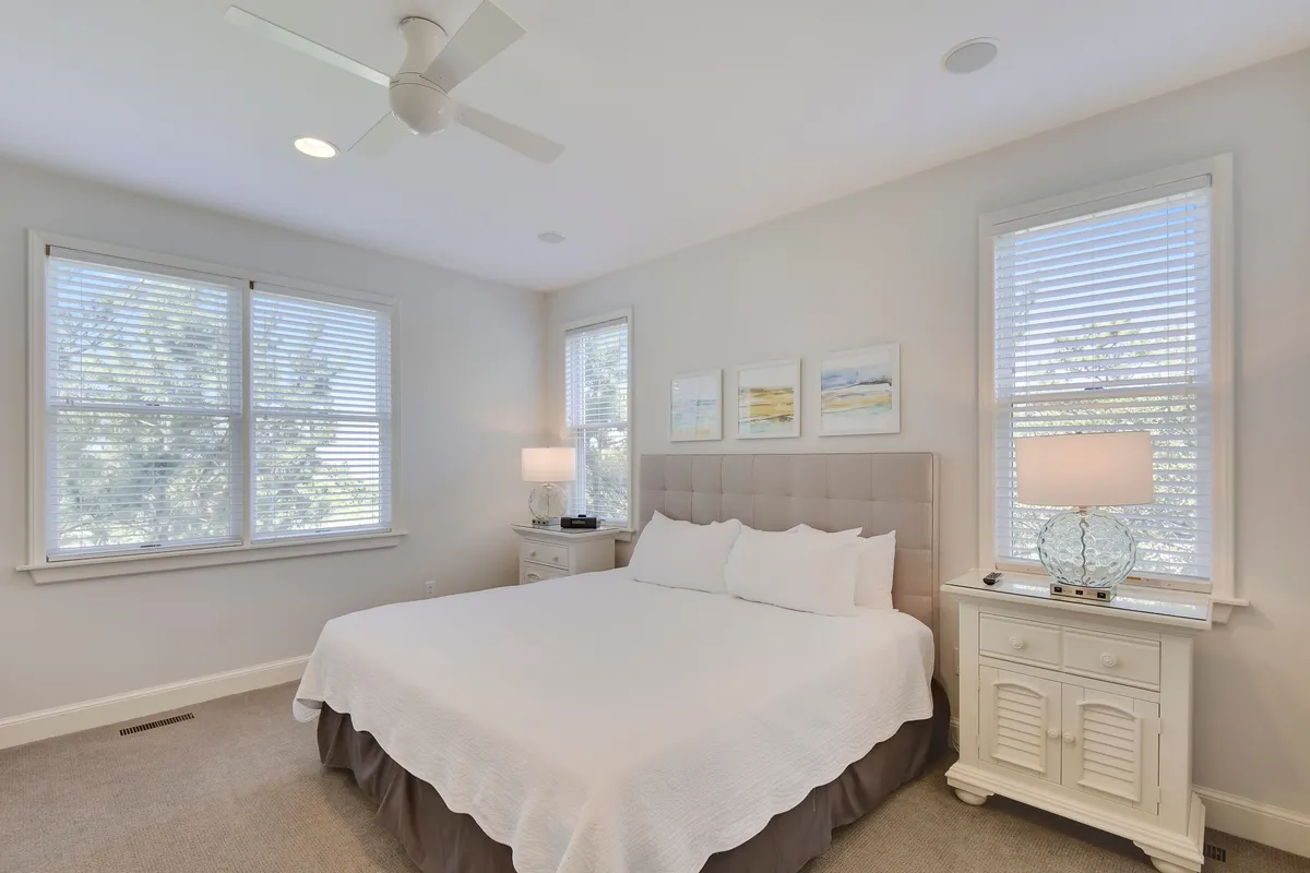 A tranquil king bedroom with a large bed, sunlight gently filtering through the windows, a cozy nightstand, and tasteful artwork. The serene color palette and soft textures evoke comfort and restful nights.