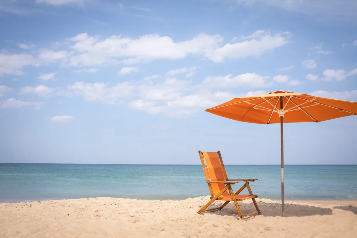 A sun-drenched beach scene featuring a beach chair and umbrella facing the gentle surf, with the ocean extending to the horizon. The setting is peaceful and inviting, suggesting a space for private reflection or a soothing start to the day.