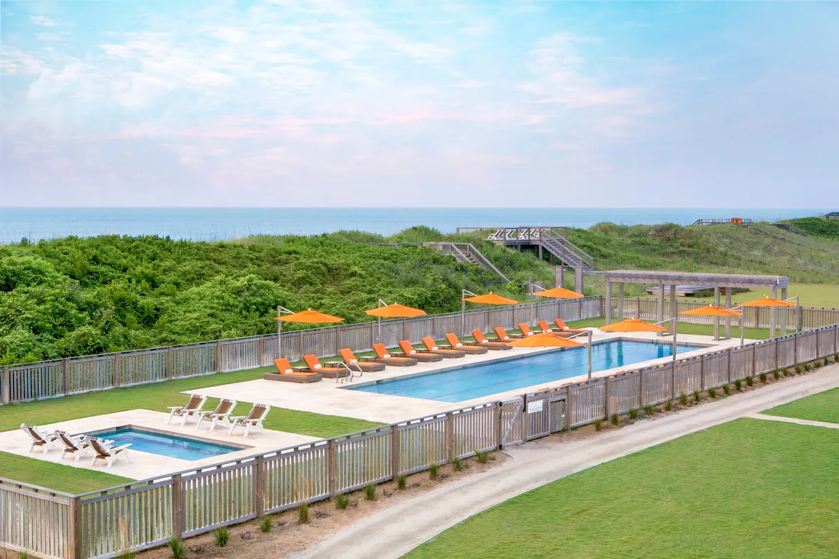 A serene outdoor swimming pool area with lounge chairs and umbrellas, offering a sweeping ocean view and surrounded by lush green landscaping. The tranquil ambiance invites relaxation and social gatherings, perfectly reflecting the resort's luxurious poolside amenities.