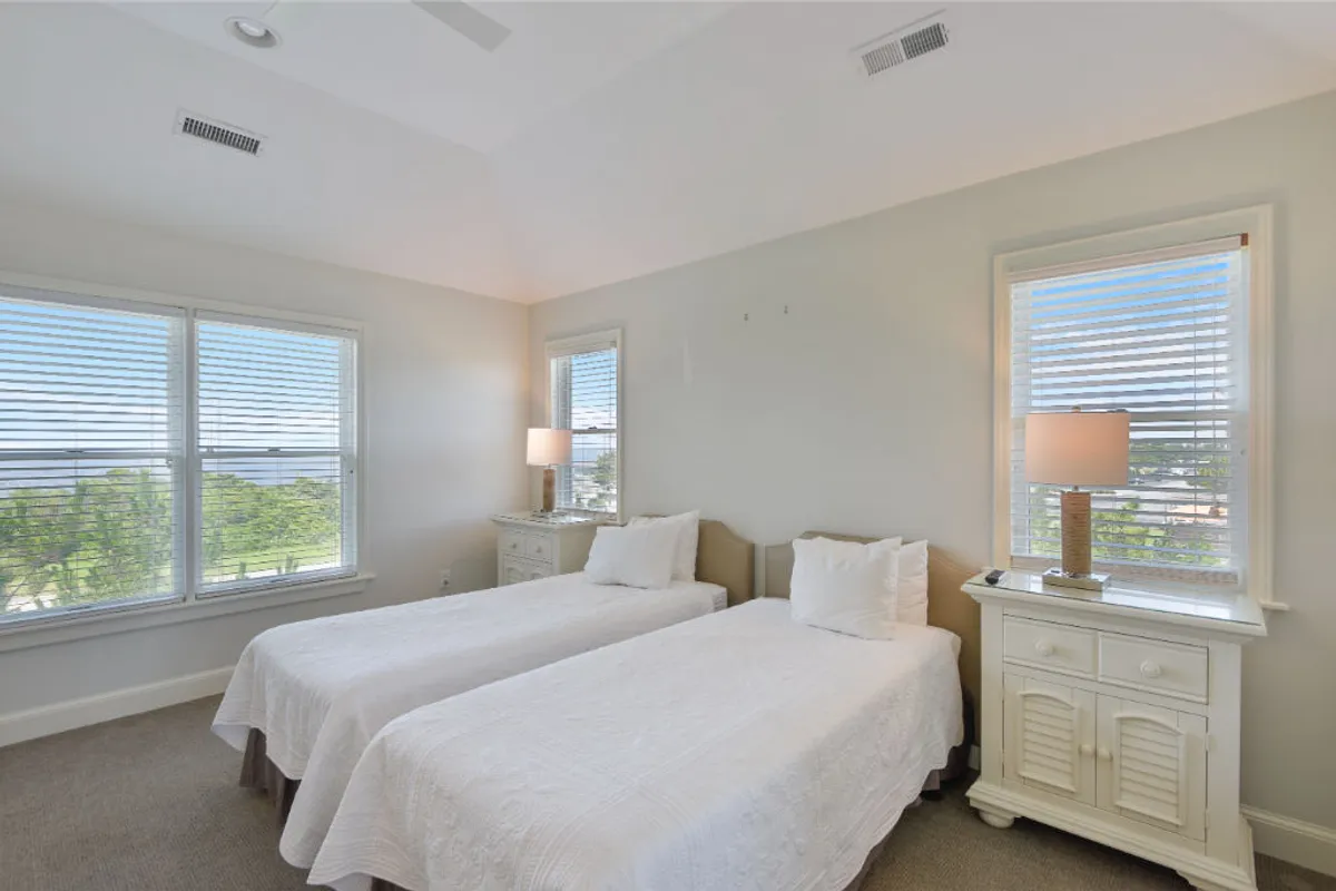 A cheerful twin bedroom featuring two inviting beds, a shared nightstand with a lamp, and windows that fill the space with morning light. The setup is perfect for guests or children, providing both comfort and a sense of fun.